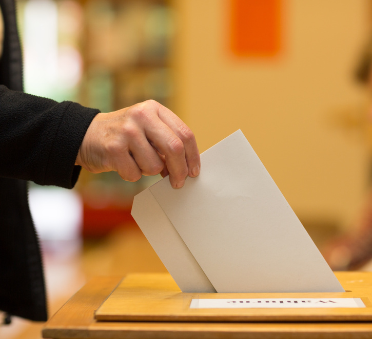 Hand mit Stimmzettel an Wahlurne